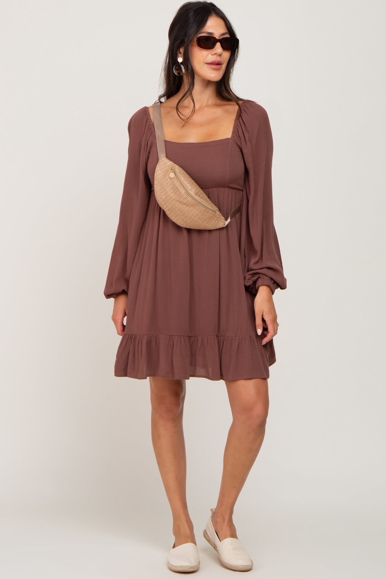 woman wearing a brown square neck long sleeve dress with a ruffled hem and a tan crossbody bag
