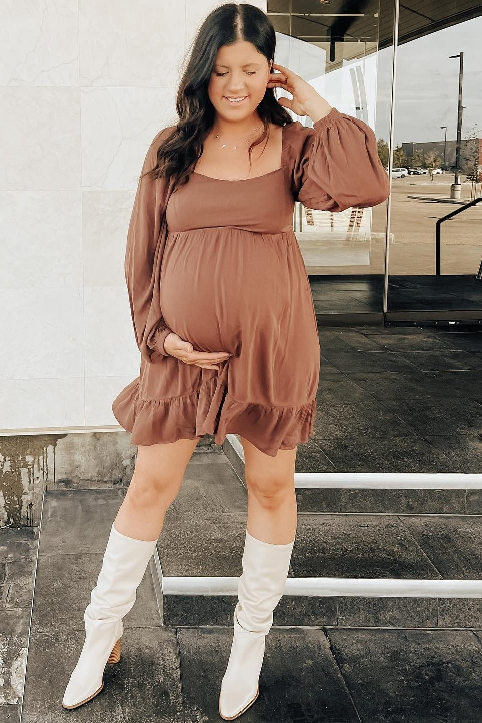 woman wearing a brown maternity dress with long sleeves and ruffle hem, showcasing her baby bump while standing outdoors