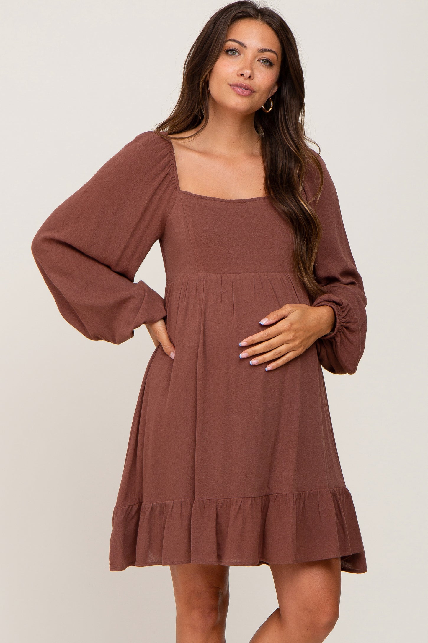 woman wearing a brown maternity dress with a square neckline and long sleeves, highlighting her baby bump
