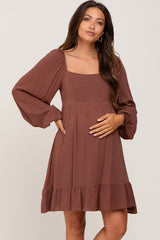 woman wearing a brown maternity dress with a square neckline and long sleeves, highlighting her baby bump