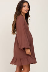 woman wearing a brown maternity dress with long sleeves and a ruffled hem, showing her baby bump