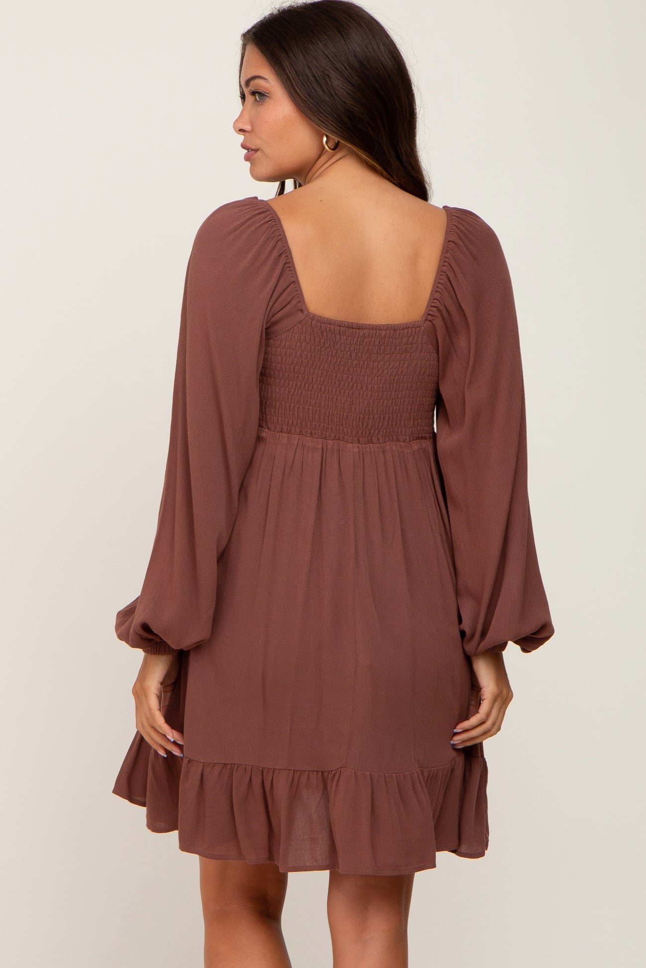 woman wearing a rust-colored long sleeve maternity dress with a smocked bodice and ruffle hem