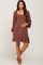 woman wearing a brown maternity dress with a square neckline, long sleeves, and ruffled hem, showing her baby bump