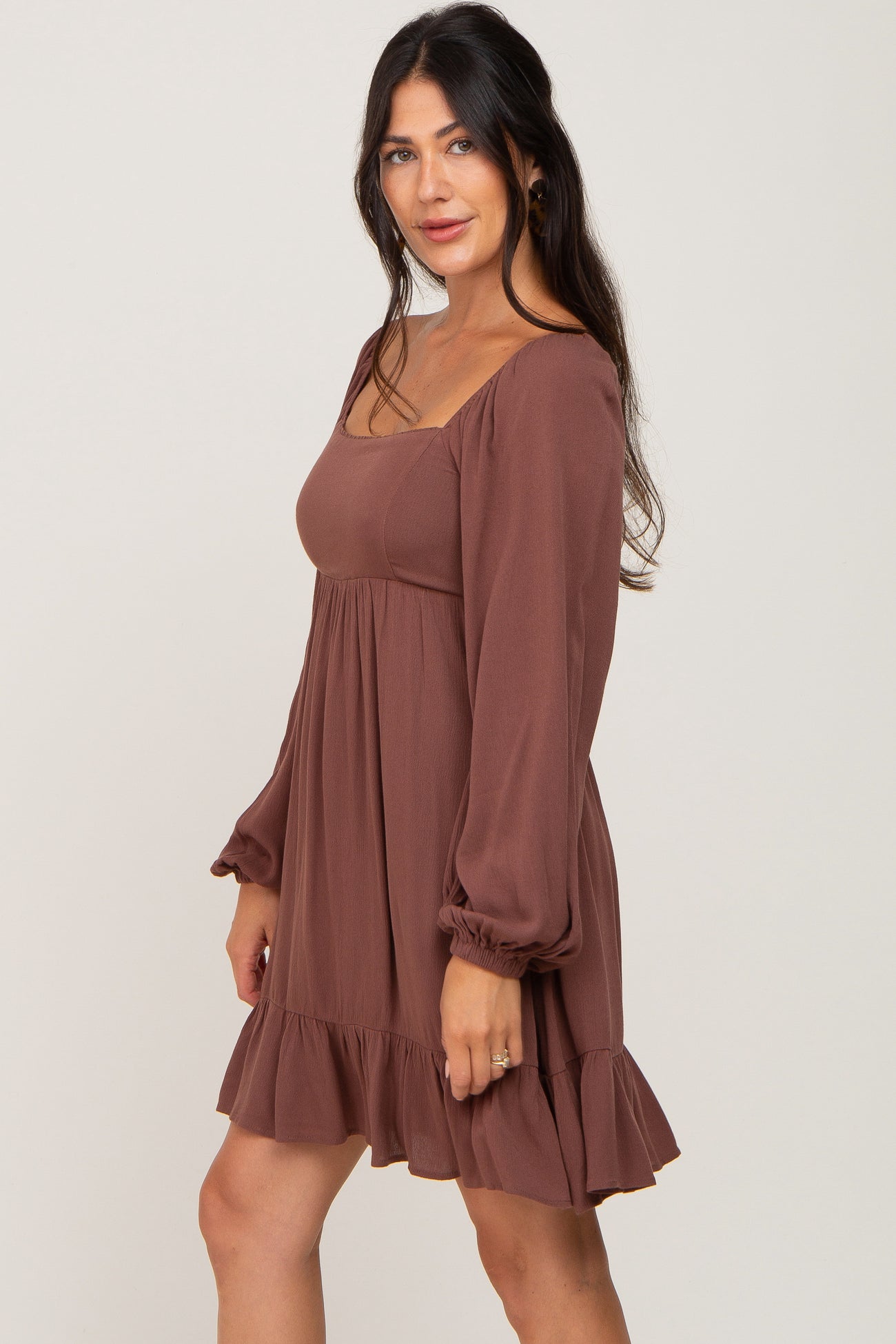 woman wearing a brown long sleeve mini dress with a ruffled hem and a square neckline