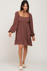 woman wearing a brown long sleeve mini dress with a square neckline and ruffle hem
