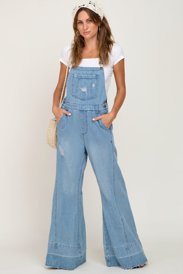 woman wearing light wash distressed denim overalls with wide legs and a white t-shirt