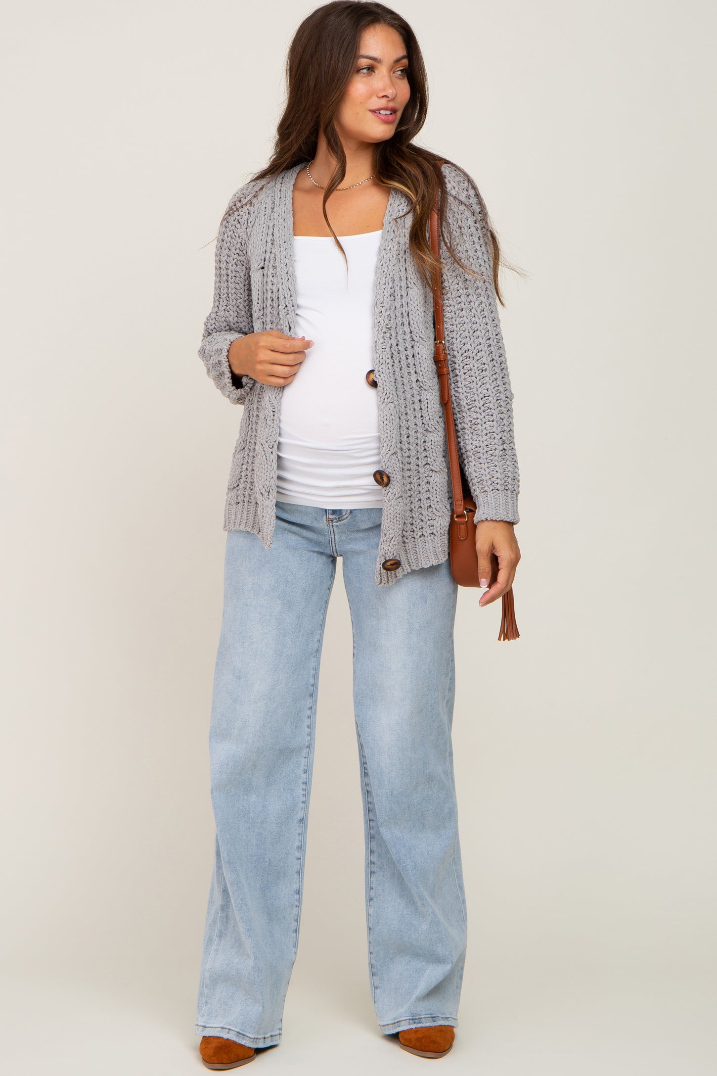 woman wearing a gray knitted maternity cardigan over a white top, paired with light blue wide-leg jeans and holding a bag