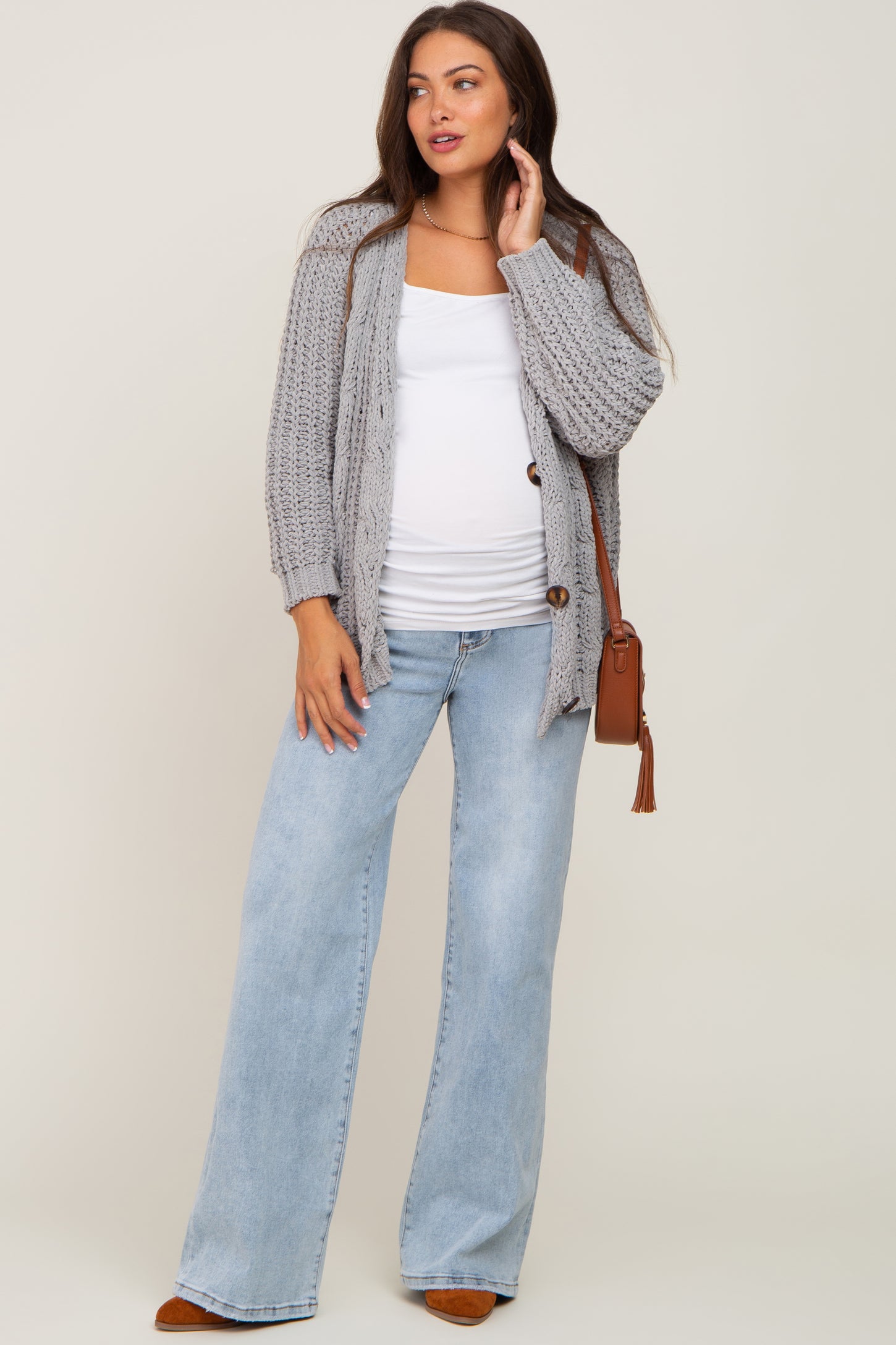 woman wearing a grey knit maternity cardigan over a white tank top, paired with light blue wide-leg jeans and a crossbody bag