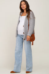 woman wearing a gray knit maternity cardigan over a white tank top and light wash wide-leg jeans, holding a brown handbag