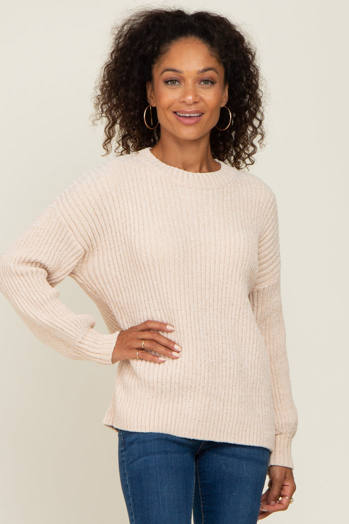 Woman with curly hair wearing a cream ribbed knit sweater and blue jeans against a neutral background