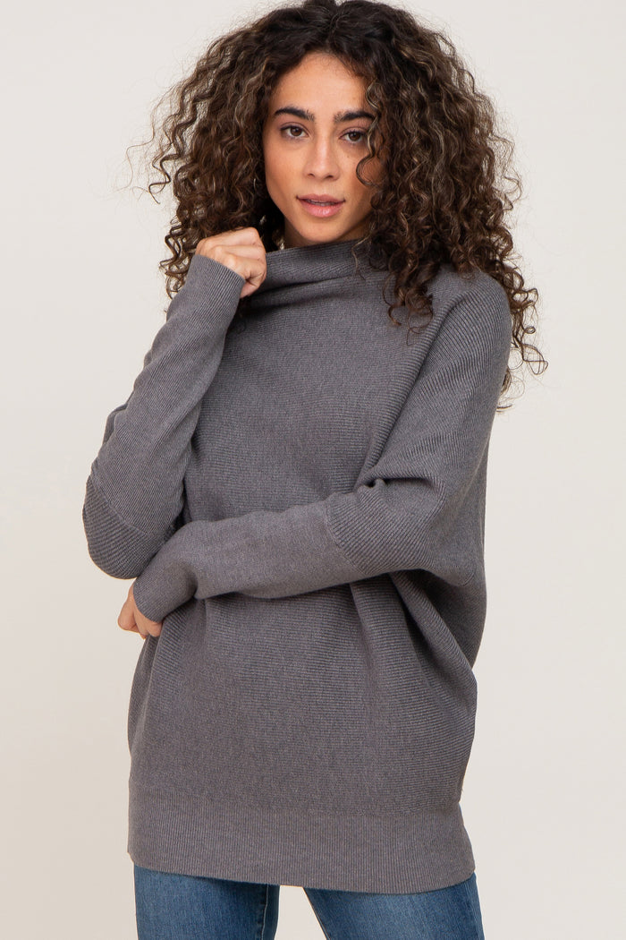 woman with curly hair wearing a grey oversized turtleneck sweater and blue jeans