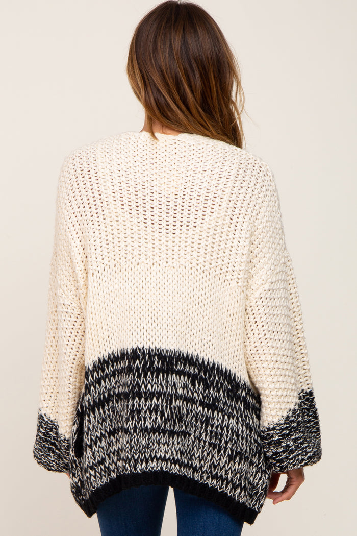 Back view of a woman wearing a cream and black colorblock chunky knit cardigan sweater