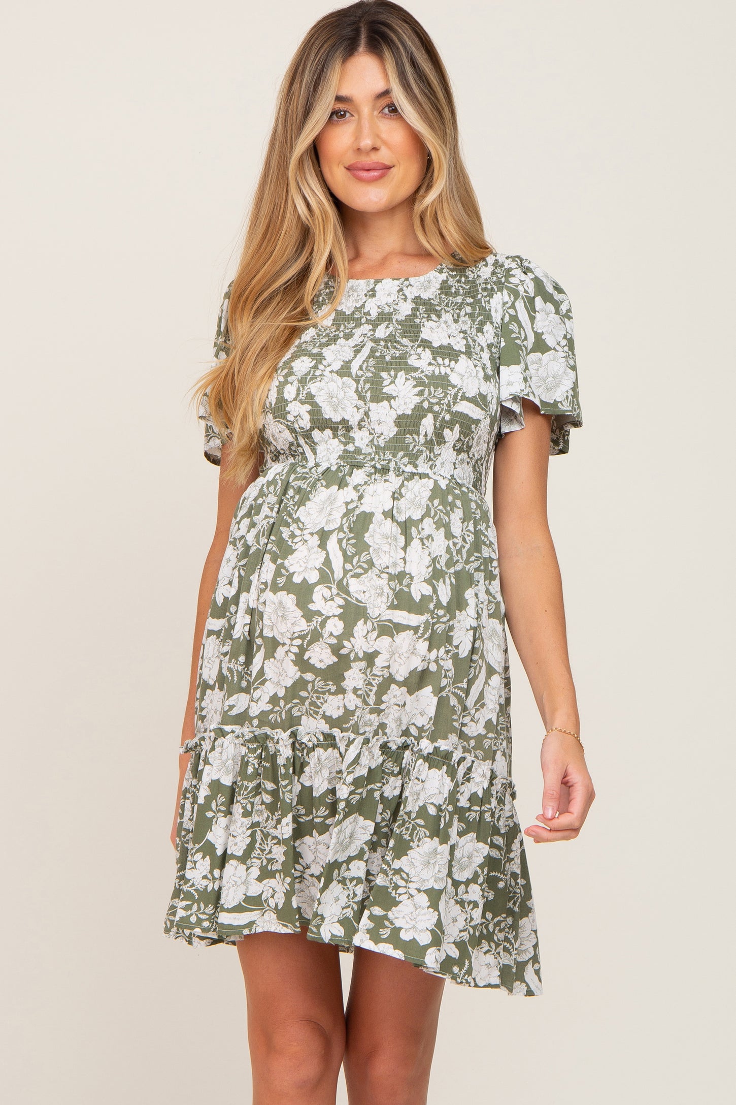 woman wearing a green floral maternity dress with puff sleeves and a tiered skirt, showcasing her baby bump