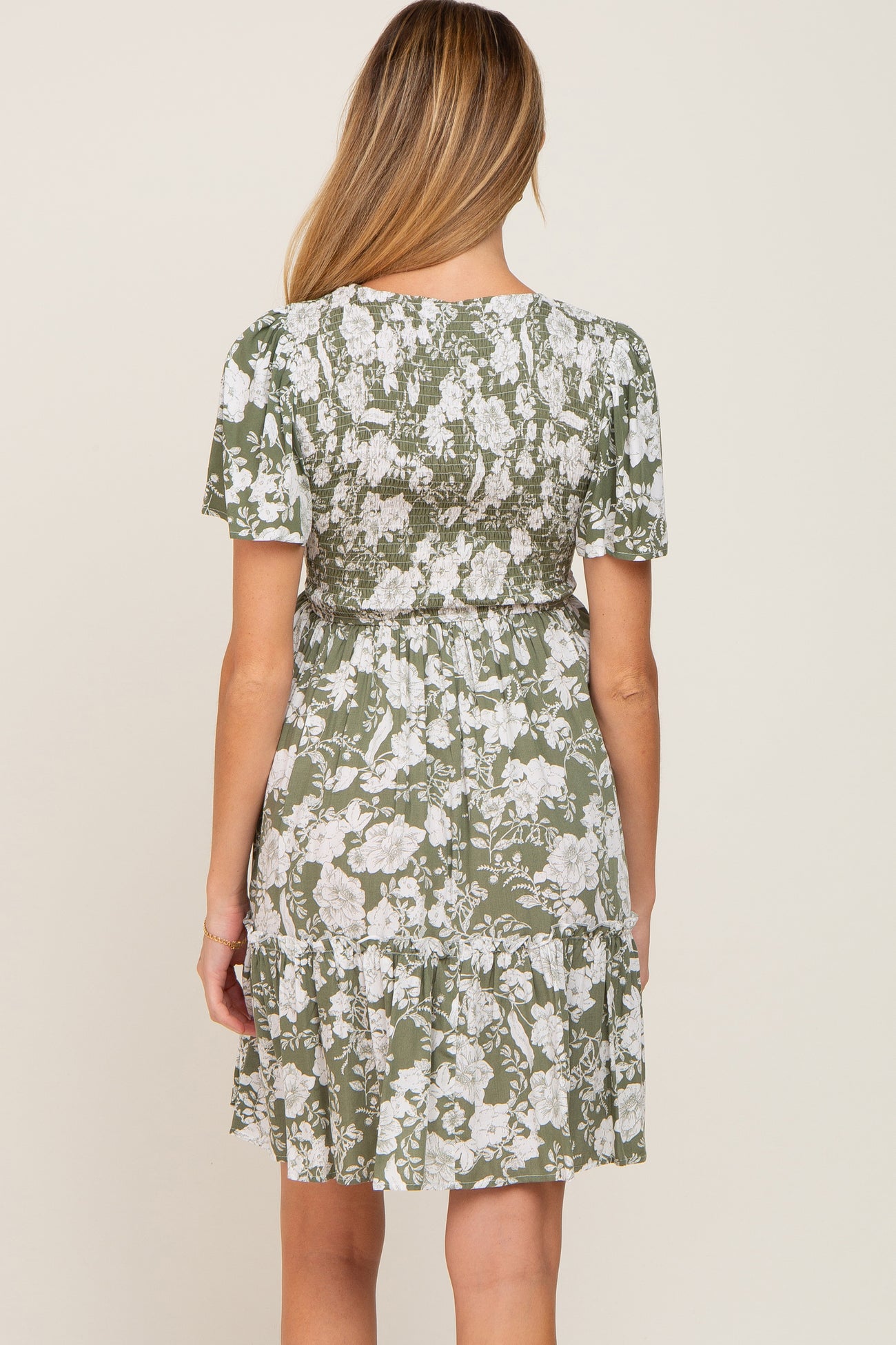 woman wearing a green floral maternity dress with short sleeves and a tiered skirt, showing her baby bump from the back