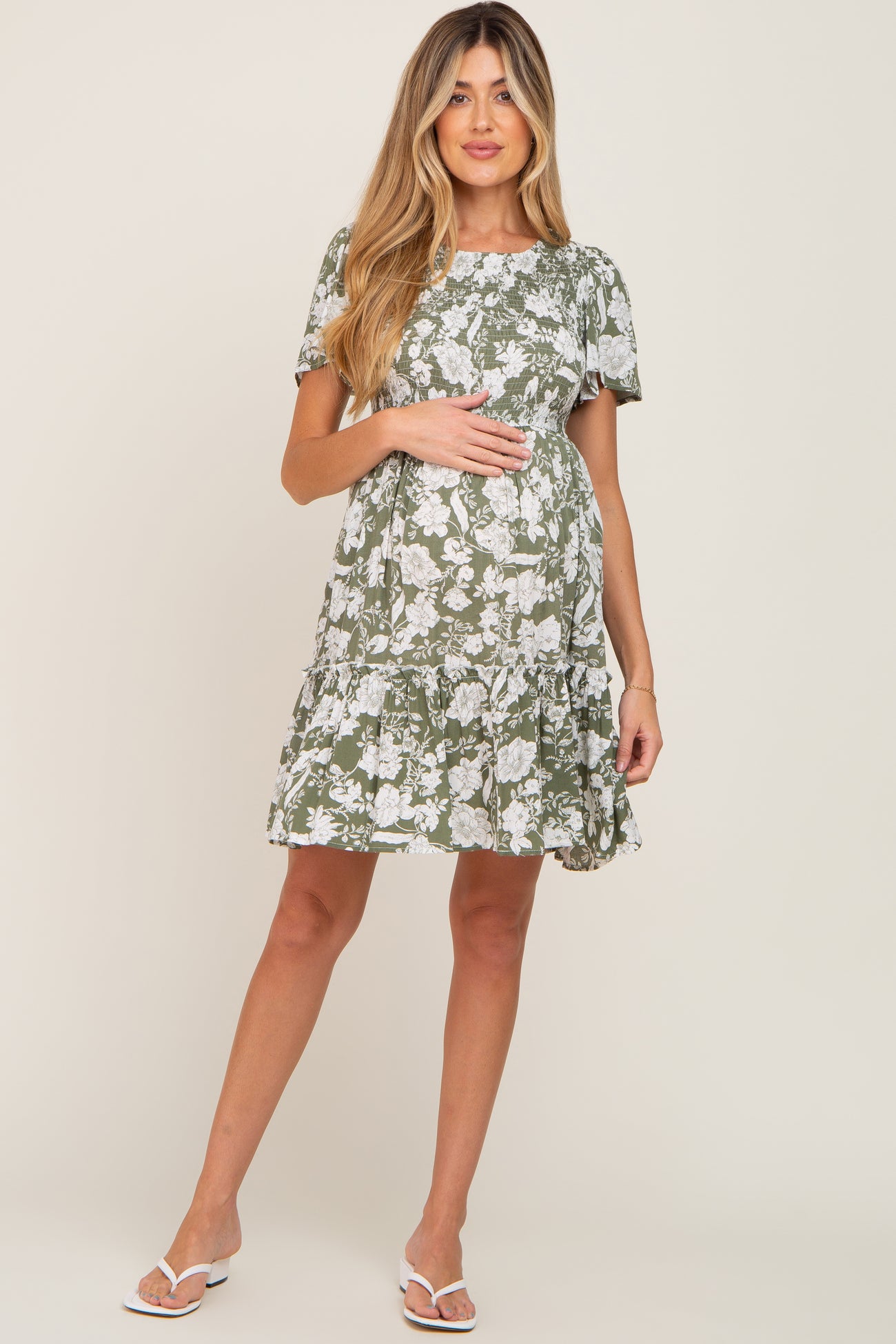 woman wearing a green floral maternity dress with a ruffled hem and holding her baby bump