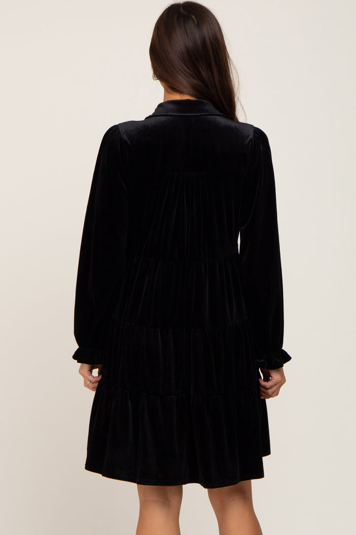 Back view of a woman wearing a black long-sleeve tiered velvet mini dress with a collar