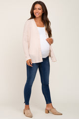 woman wearing a light pink maternity cardigan over a white top and blue maternity jeans, showing her baby bump