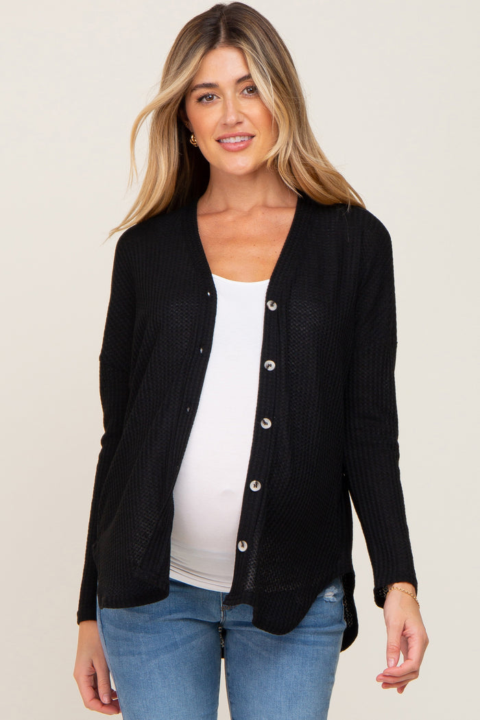 woman wearing a black button-up maternity cardigan over a white top and showing her baby bump