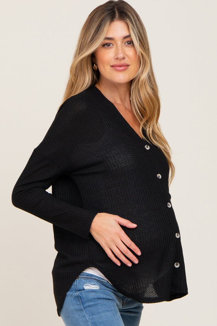 woman wearing a black maternity cardigan with buttons, posing with her baby bump visible, paired with light blue jeans