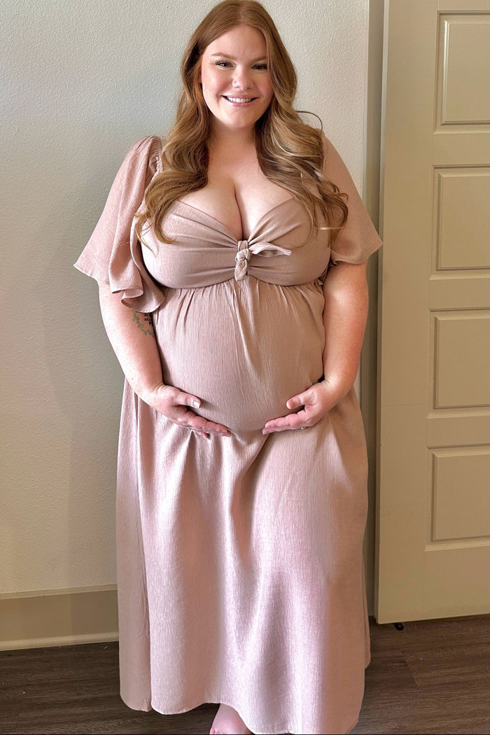 smiling pregnant woman with long red hair wearing a mauve maternity maxi dress holding her baby bump