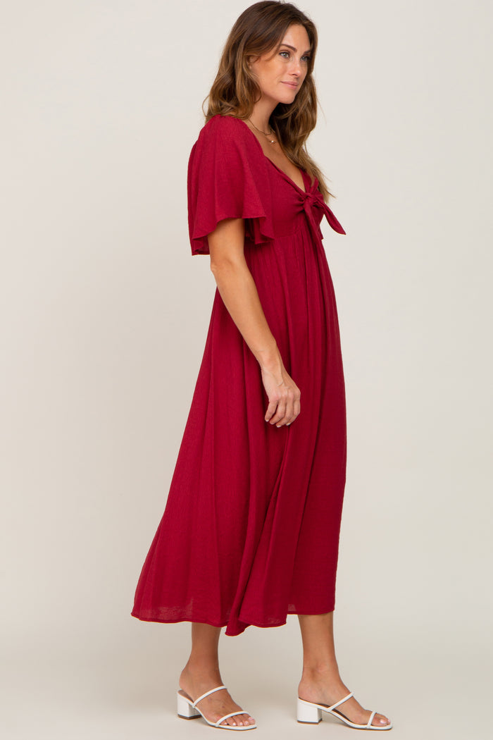 woman wearing a deep red flutter sleeve maxi dress with a tie front detail