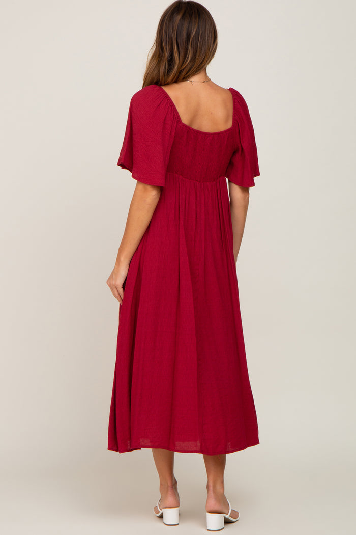 woman wearing a burgundy midi dress with short flutter sleeves and a square back design