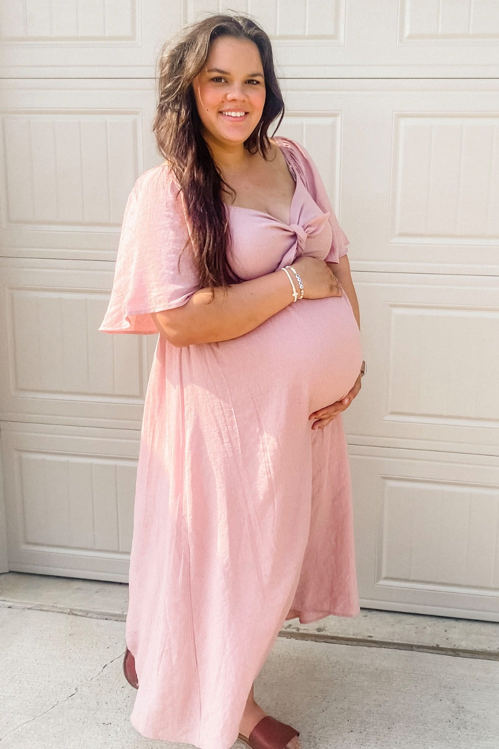 woman wearing a light pink maternity dress with short flutter sleeves and holding her baby bump