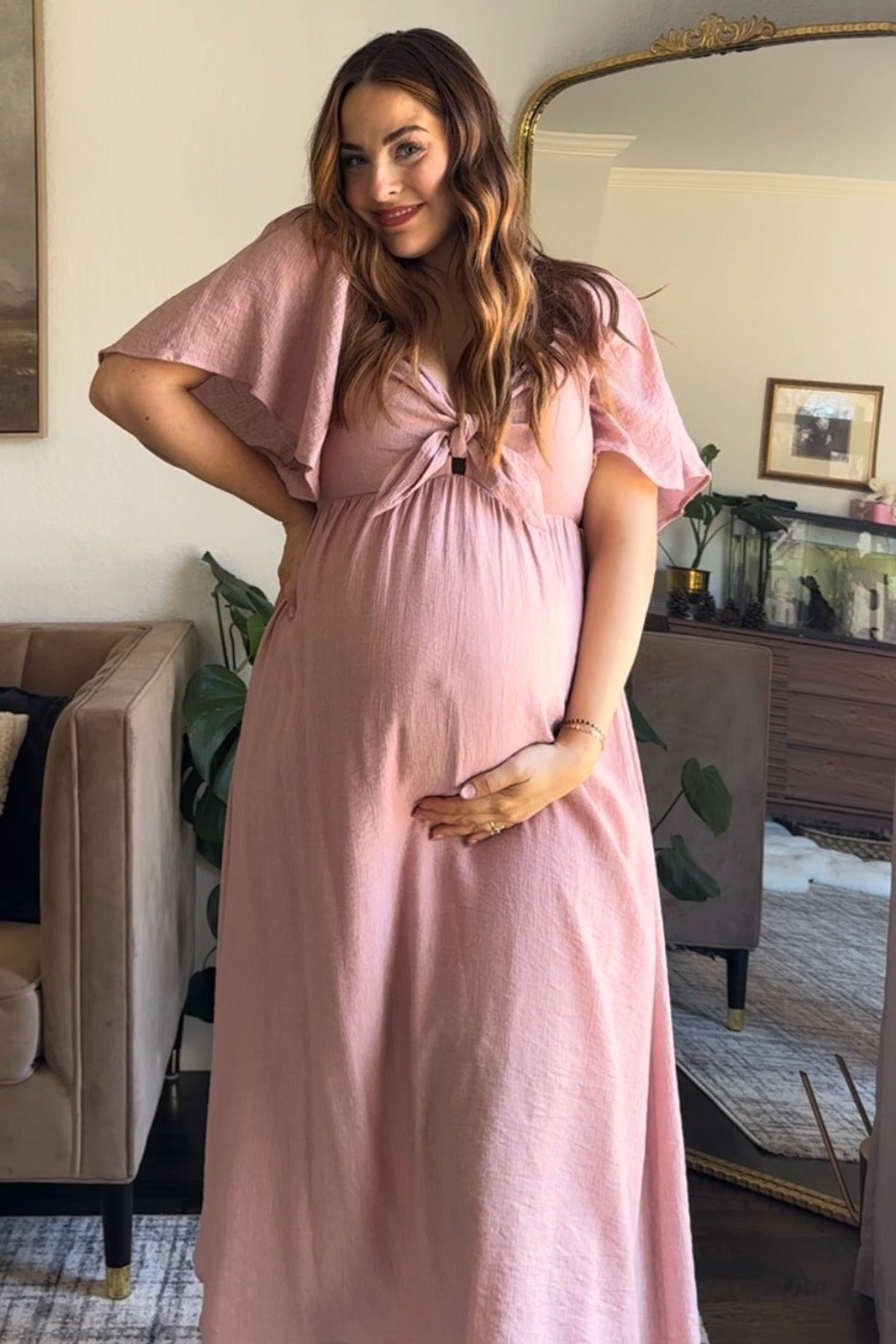 woman wearing a light pink maternity maxi dress with a tie front and holding her baby bump