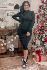 woman wearing a black long sleeve fitted dress and stylish sneakers, posing beside a decorated Christmas tree