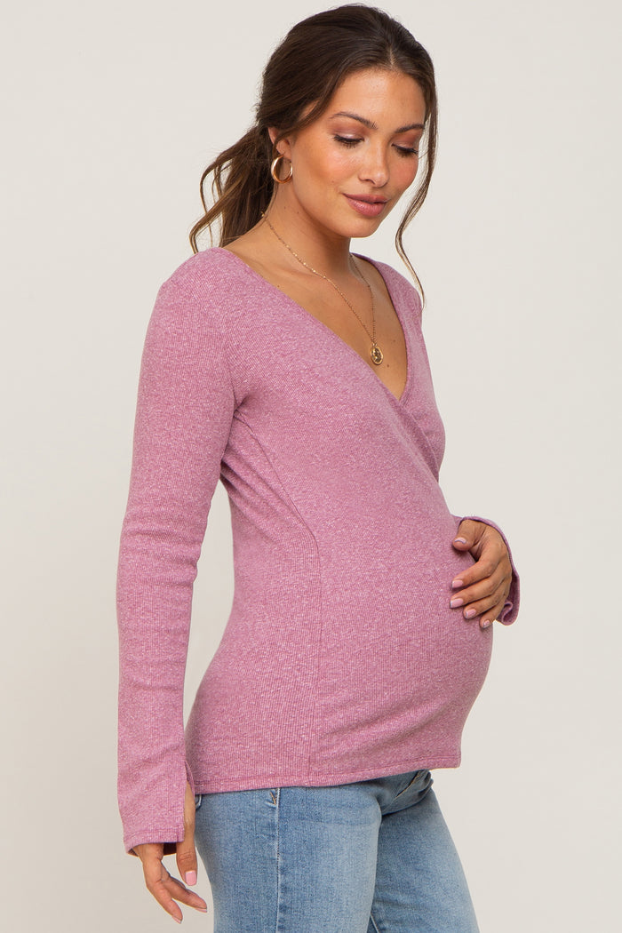 woman wearing a pink long sleeve maternity top and gently holding her baby bump