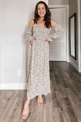 woman wearing a floral off-the-shoulder maxi dress with puff sleeves and pockets, smiling in a bright interior
