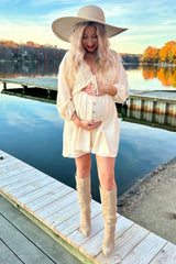 woman wearing a cream maternity dress with buttons and lace detailing, cradling her baby bump by a lake