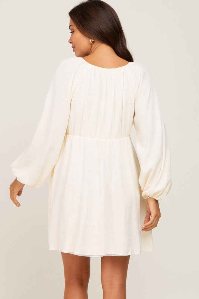 woman wearing a cream maternity dress with long balloon sleeves and a fitted waist, showing a modest back view