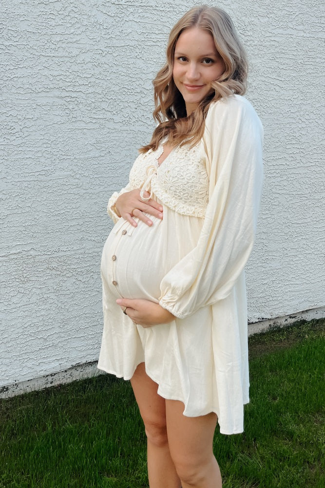 woman wearing a cream maternity dress with lace details and puff sleeves, cradling her baby bump