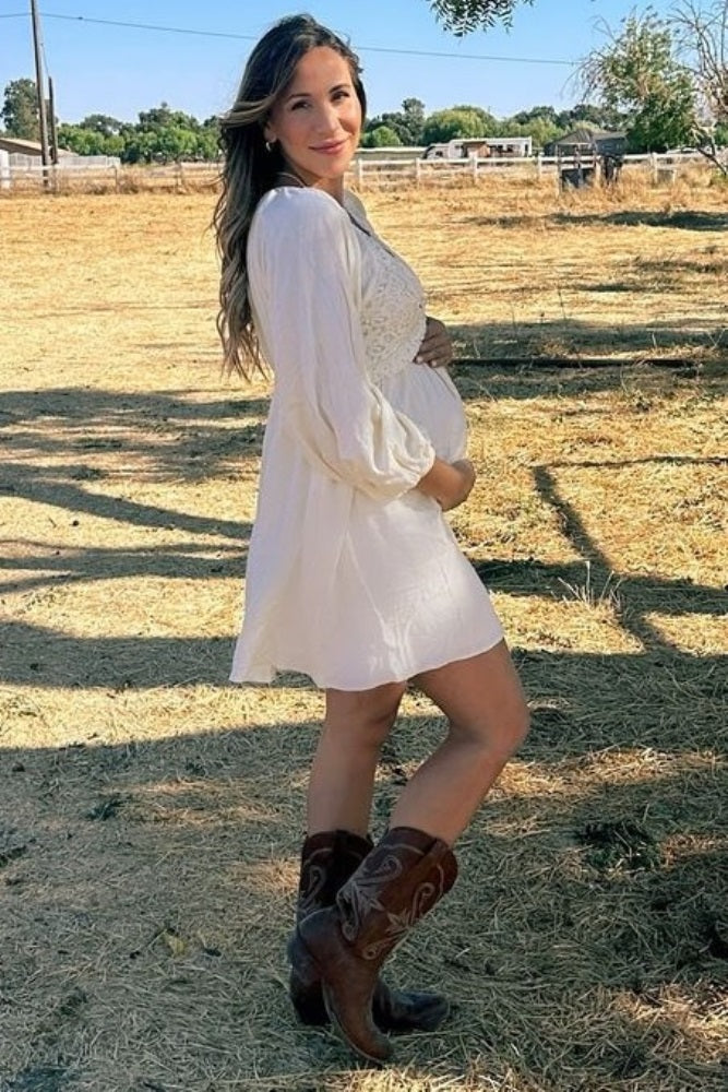woman wearing a white maternity dress with puff sleeves and holding her baby bump in a rural setting