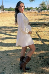 woman wearing a white maternity dress with puff sleeves and holding her baby bump in a rural setting