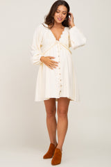 woman wearing a cream maternity dress with lace detailing and buttons, holding her baby bump