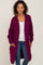 woman wearing a magenta long cardigan with pockets over a white top and blue jeans