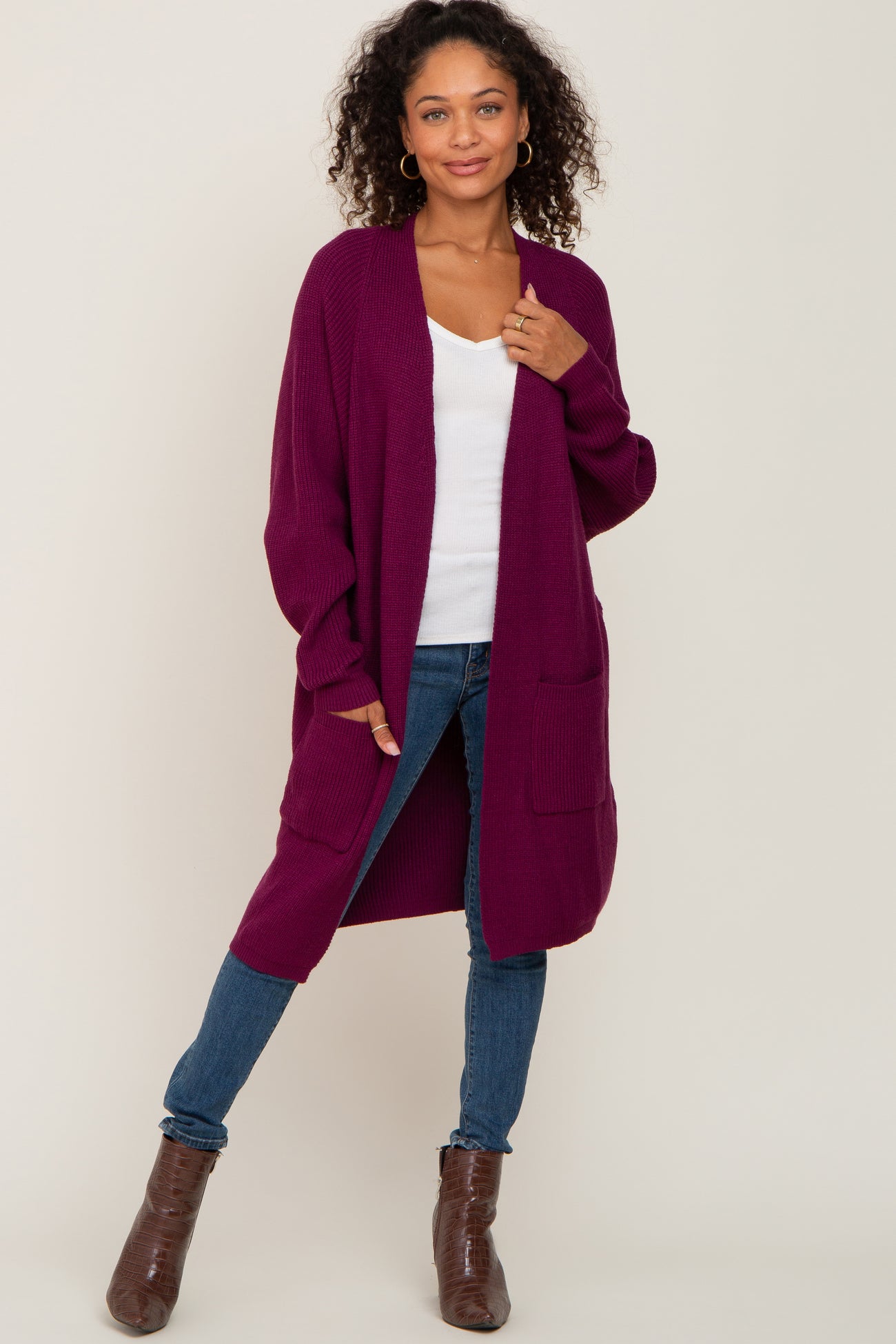 woman wearing a burgundy long cardigan with two front pockets over a white tank top and blue jeans