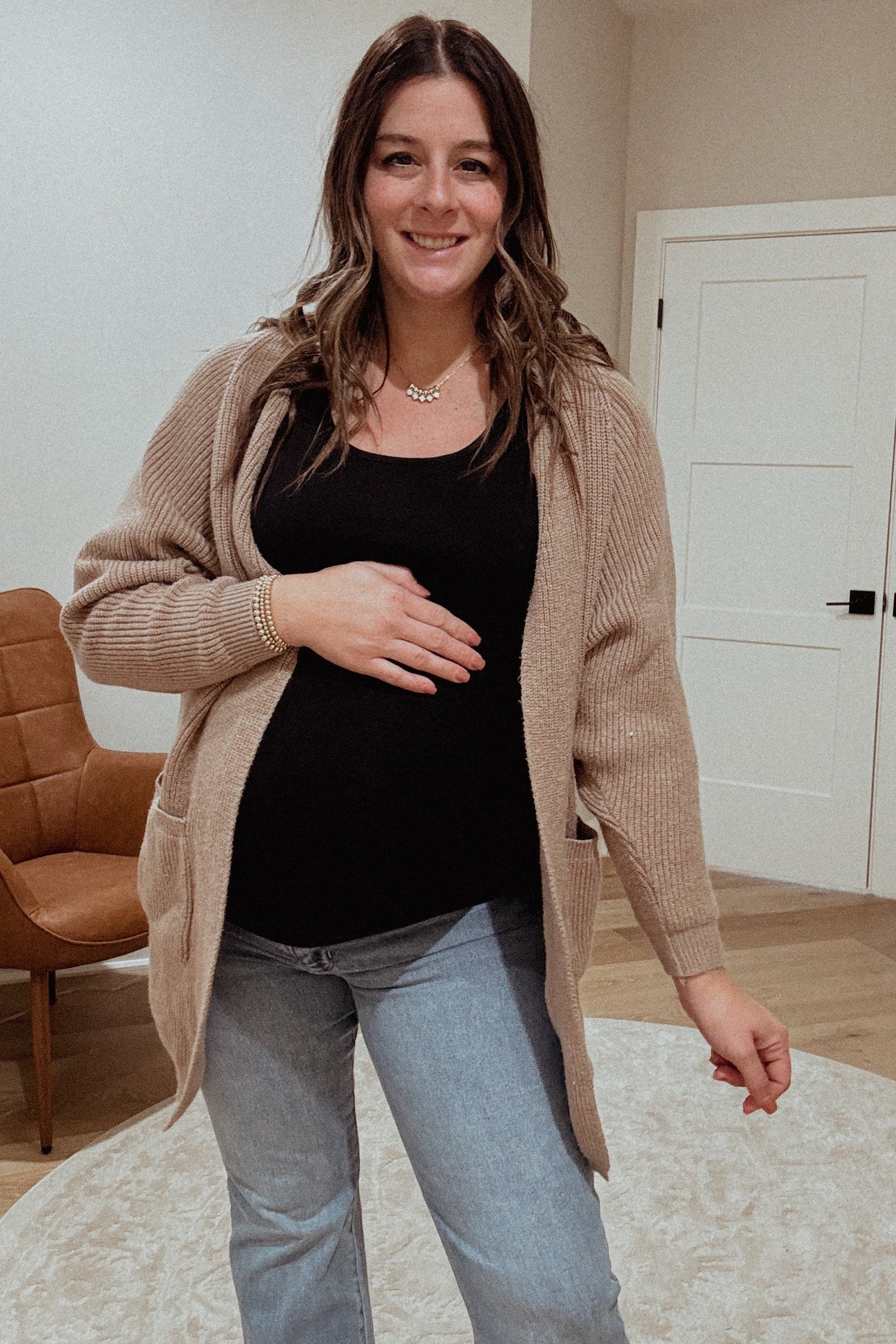 woman wearing a beige knitted cardigan over a black top and jeans, showing her baby bump