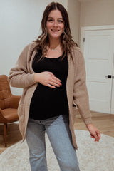 woman wearing a beige knitted cardigan over a black top and jeans, showing her baby bump