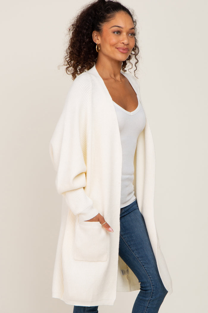 woman wearing a cream long cardigan with oversized sleeves and front pockets over a white tank top and blue jeans