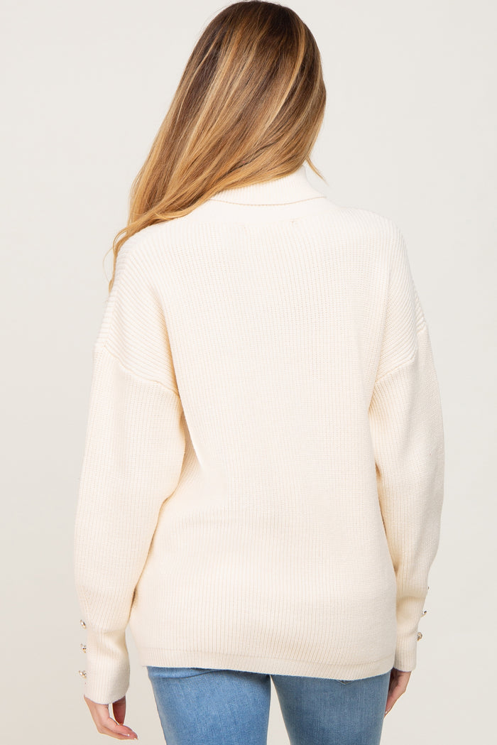 woman wearing a cream oversized maternity sweater with ribbed texture and button details at the cuffs