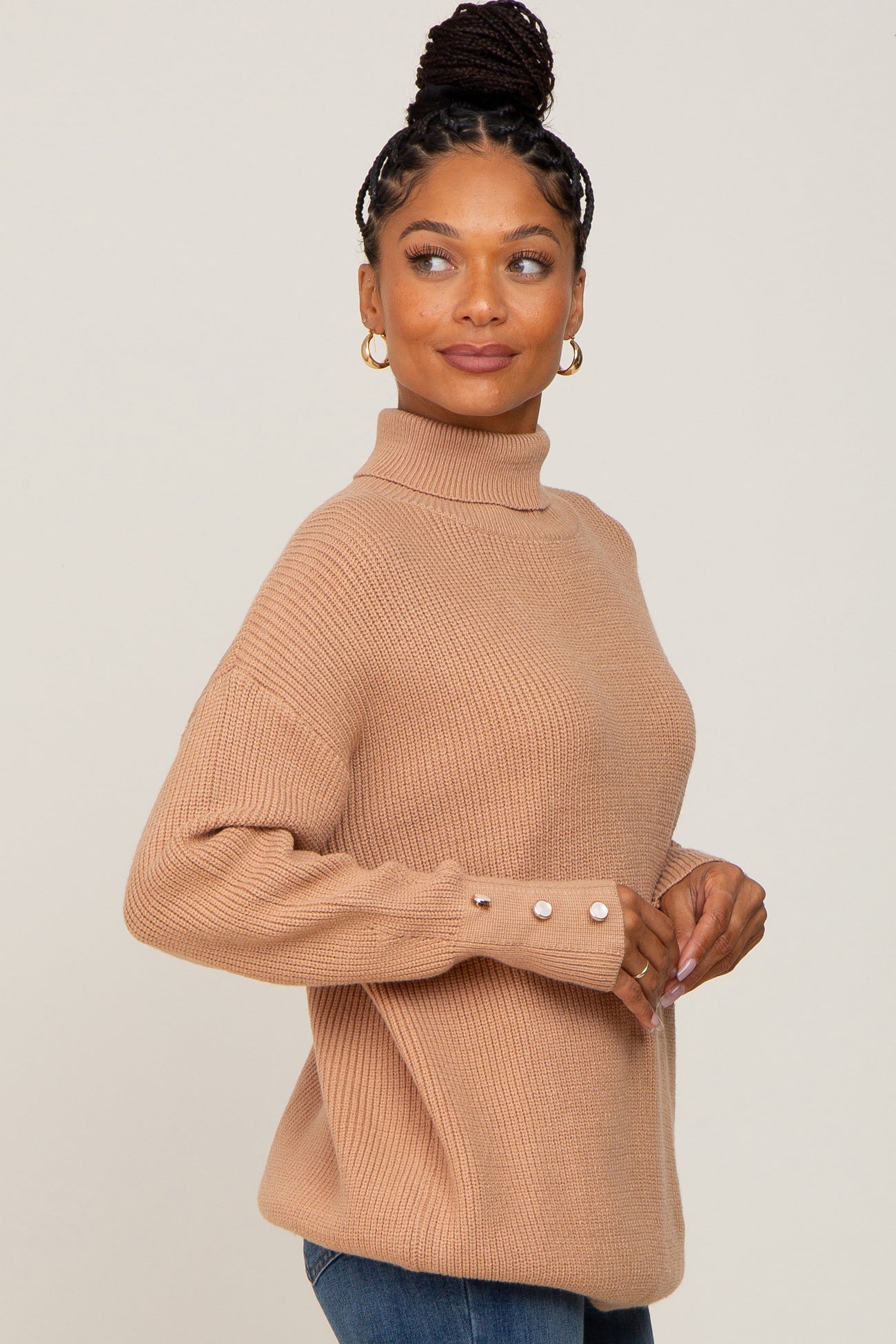 woman wearing a tan ribbed turtleneck sweater with button details on the sleeves and styled with blue jeans