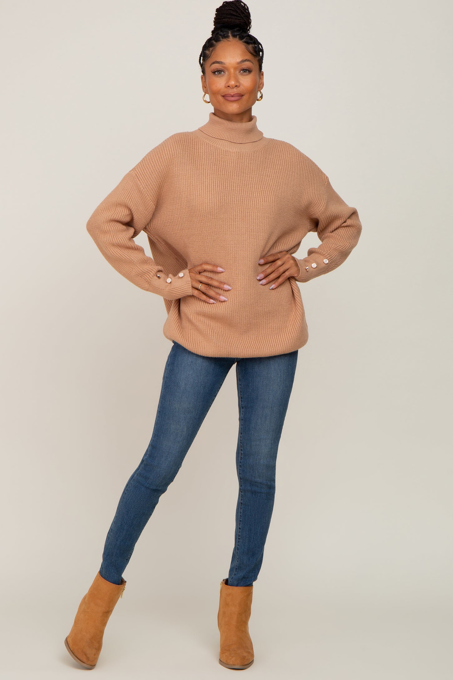 woman wearing a beige chunky knit sweater with button details and blue skinny jeans, standing in brown ankle boots