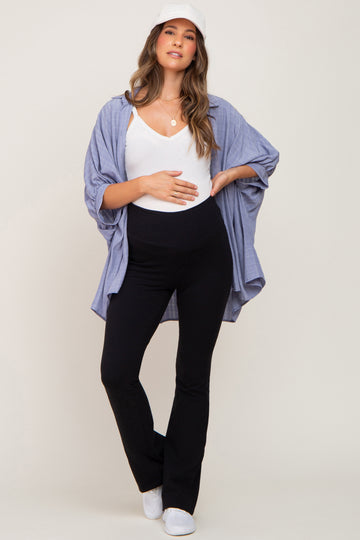 woman wearing a white maternity tank top, black maternity flared pants, and a blue button-up shirt, holding her baby bump