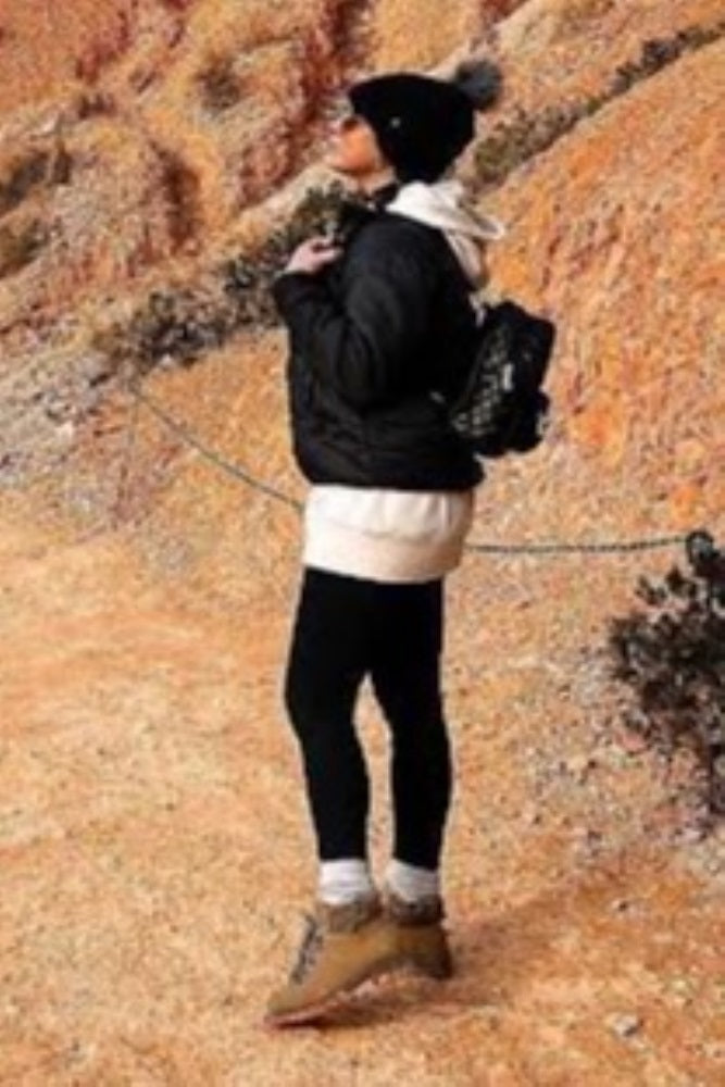person in winter hiking gear with black jacket and beanie standing on a rocky trail