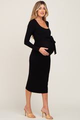Pregnant woman wearing a long sleeve black maternity midi dress with a waist tie and tan heels