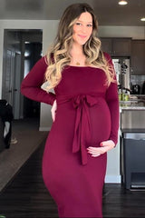 woman wearing a burgundy long sleeve maternity dress with a tie waist and holding her baby bump