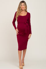 woman wearing a burgundy long sleeve maternity dress with a tie waist and a visible baby bump